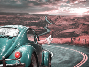 passenger with feet hanging out the window of a Vintage VW on a Windy country road