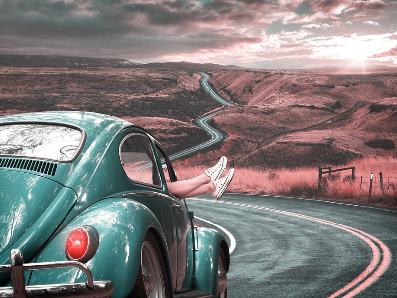 passenger with feet hanging out the window of a Vintage VW on a Windy country road